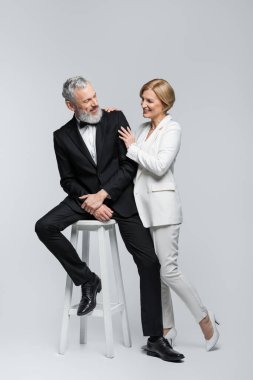 Gülümseyen olgun gelin zarif damadı kucaklıyor gri arka planda sandalyede oturuyor. 