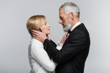 Resmi giyinmiş olgun damadın yan görünüşü Gri renkte izole edilmiş sarışın geline dokunmak 