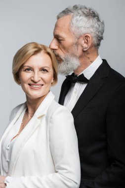 Gri renkte izole edilmiş gülümseyen gelinin başıyla öpüşen olgun damadın portresi. 