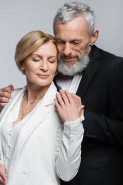 Sakallı damat portresi. Gözleri kapalı, gelinine sarılan gri elbiseli. 