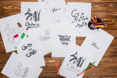 top view of white paper sheets with various fonts, color pencils and felt pens on wooden surface clipart
