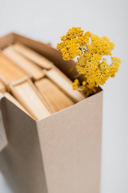 Bulanık alışveriş çantasının yakınındaki kurutulmuş sarı çiçeklerin seçici odağı.