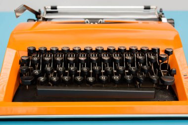 close up view of bright orange typewriter with black keyboard isolated on blue clipart