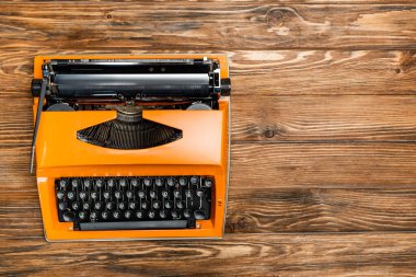 top view of orange typewriter on brown wooden surface clipart