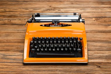 bright orange typewriter with black keyboard on textured wooden surface clipart