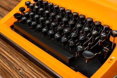 close up view of black keyboard of orange typewriter on wooden surface clipart