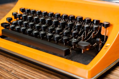 close up view of orange typewriter with black keyboard on wooden desk clipart