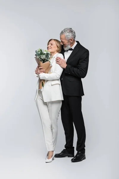Maturo Sposo Abbracciare Sposa Allegra Con Bouquet Sfondo Grigio — Foto Stock