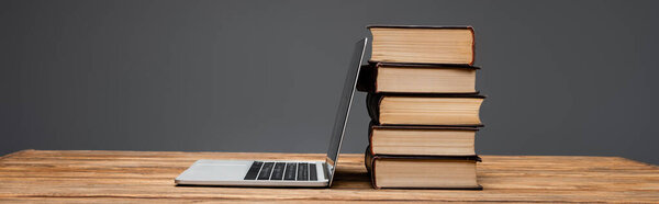 stack of books and laptop on wooden desk isolated on grey, banner
