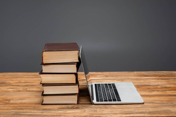 laptop near books stacked on wooden desk isolated on grey