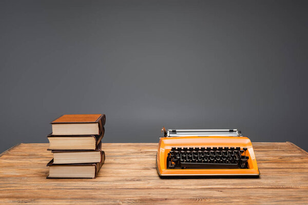 orange typewriter and stack of books on wooden desk isolated on grey