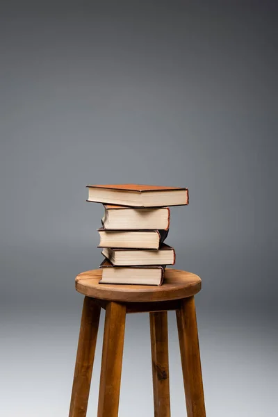 灰色の背景に茶色の木製のスツールに関する本の山 — ストック写真