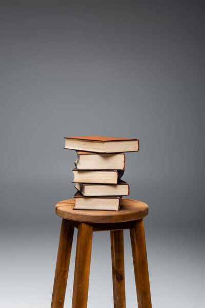 pile of books on brown wooden stool on grey background