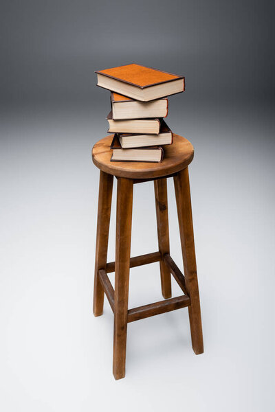 wooden stool with pile of books on grey background