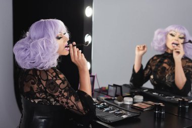 Aynanın yanında kozmetik fırçasıyla oturan eksantrik travesti