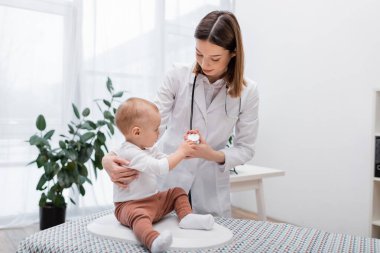 Klinikte elektronik ölçekte otururken bebeğin steteskopa dokunması 