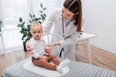 Neşeli doktor bebeği klinikte elektronik ölçekte tutuyor. 
