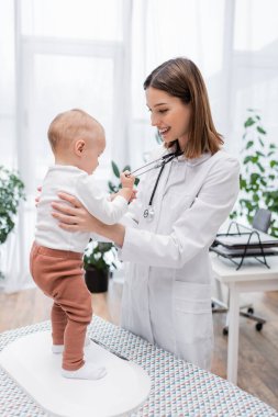 Pozitif doktor bebeği elektronik ölçekte tutuyor.