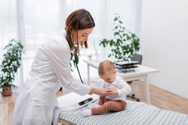 Esmer doktor hastanede steteskopla bebeği muayene ediyor. 