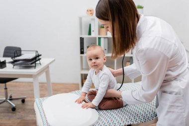 Genç bir aile doktoru, tıbbi kanepede elektronik ölçekte bir bebeğin göğsünü inceliyor. 
