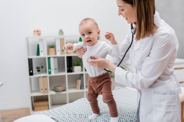 Hastanedeki tıbbi kanepede steteskopla bebeği muayene eden pozitif aile doktoru. 