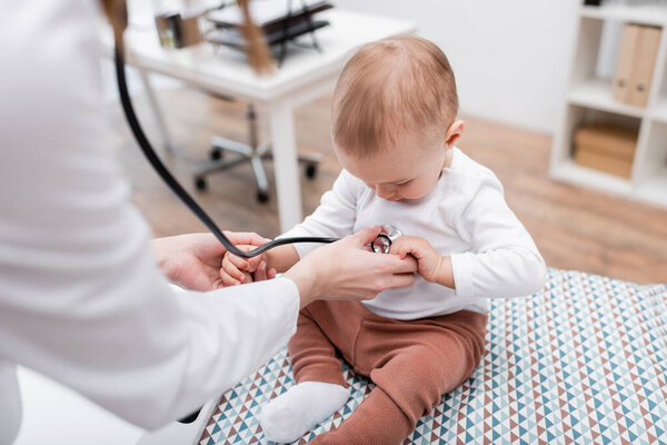 Blurred doctor examining baby with stethoscope on medical couch in clinic 