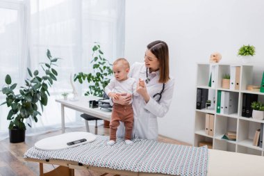 Aile doktoru bebeği klinikteki tıbbi kanepede elektronik ölçekte tutuyor. 