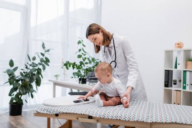 Bebek klinikteki aile doktorunun yanındaki tıbbi kanepede elektronik teraziye dokunuyor. 
