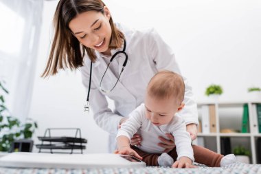 Bebek klinikteki pozitif aile doktorunun yanındaki tıbbi kanepede bulanık elektronik teraziye dokunuyor. 