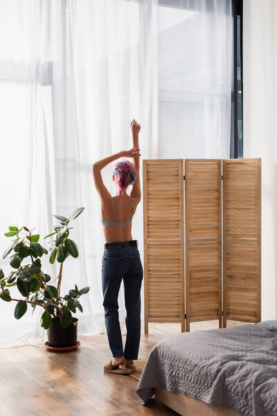 вид сзади на молодую женщину с окрашенными волосами, стоящую возле складного экрана