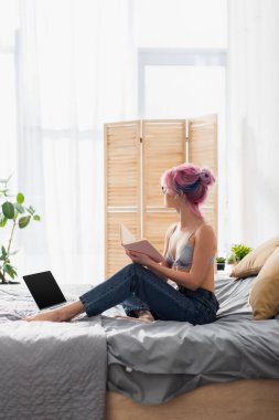 Dövmeli, saçları boyalı, elinde not defteri olan, evde internetten ders çalışan genç bir kadın.