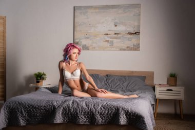 Yatakta oturan seksi iç çamaşırlı baştan çıkarıcı genç kadın.