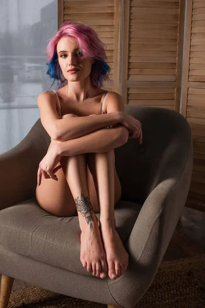 seductive young woman with tattoo sitting on armchair