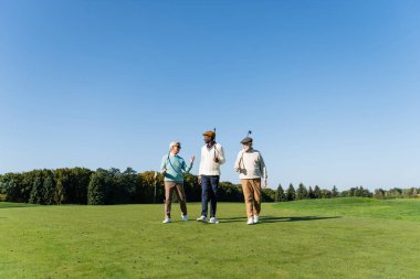 Kıdemli ırklar arası arkadaşlar golf sopalarıyla sahada yürüyorlar.