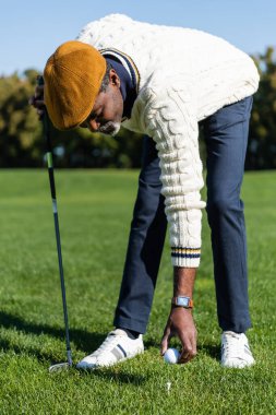 Sakallı Afrikalı Amerikalı adam golf tişörtüne top koyuyor.