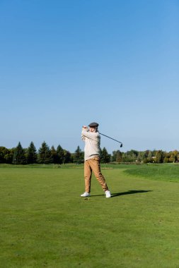 Düz şapkalı son sınıf öğrencisi yeşil çimlerde golf oynuyor. 