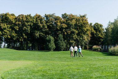 Golf sopalarıyla yeşil sahada yürüyen üst düzey çok ırklı dostların arka planı