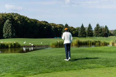 Golf sopası tutan ve yeşil alanda yürüyen Afro-Amerikan adamın arka görüntüsü. 
