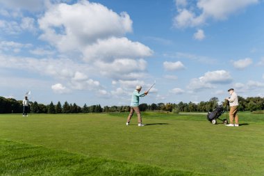 Kıdemli Asyalı adam arkadaşlarının yanında golf oynuyor bayrak sopası ve golf arabasıyla.