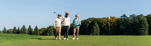 Senior Interraciale Vrienden Wandelen Met Golfclubs Groen Veld Banner — Stockfoto