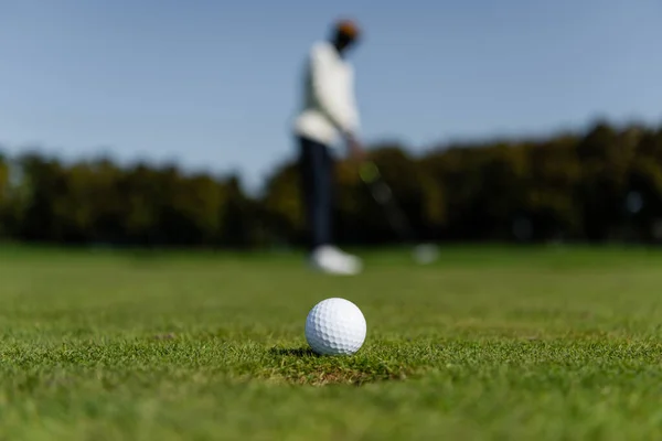 ぼやけた男の近くの緑の畑の新鮮な草の上のゴルフボール — ストック写真
