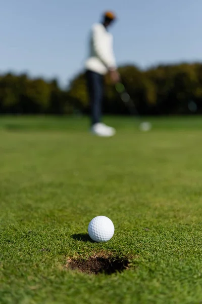 ぼやけたゴルファーの近くの緑のフィールドの芝生の上のゴルフボール — ストック写真