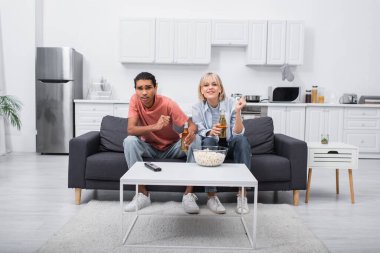 young interracial couple cheering while watching sport match in living room 