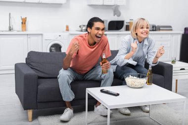 cheerful multiethnic couple cheering while watching sport match in living room 