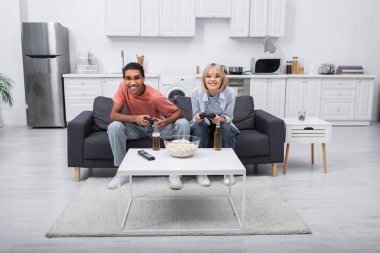 KYIV, UKRAINE - DECEMBER 6, 2021: joyful multiethnic couple playing video game in living room 