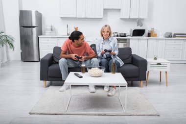 KYIV, UKRAINE - DECEMBER 6, 2021: happy interracial couple playing video game in living room 