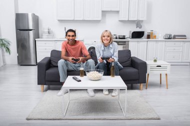 KYIV, UKRAINE - DECEMBER 6, 2021: excited multiethnic couple playing video game in living room 