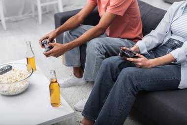 KYIV, UKRAINE - DECEMBER 6, 2021: cropped view of multiethnic couple holding joysticks and playing video game