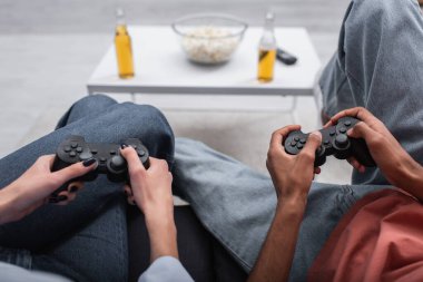 KYIV, UKRAINE - DECEMBER 6, 2021: partial view of interracial couple holding joysticks and playing video game 
