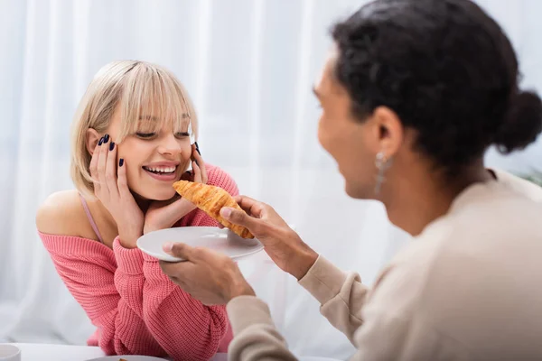 Blurred African American Man Feeding Blonde Girlfriend Croissant — стоковое фото